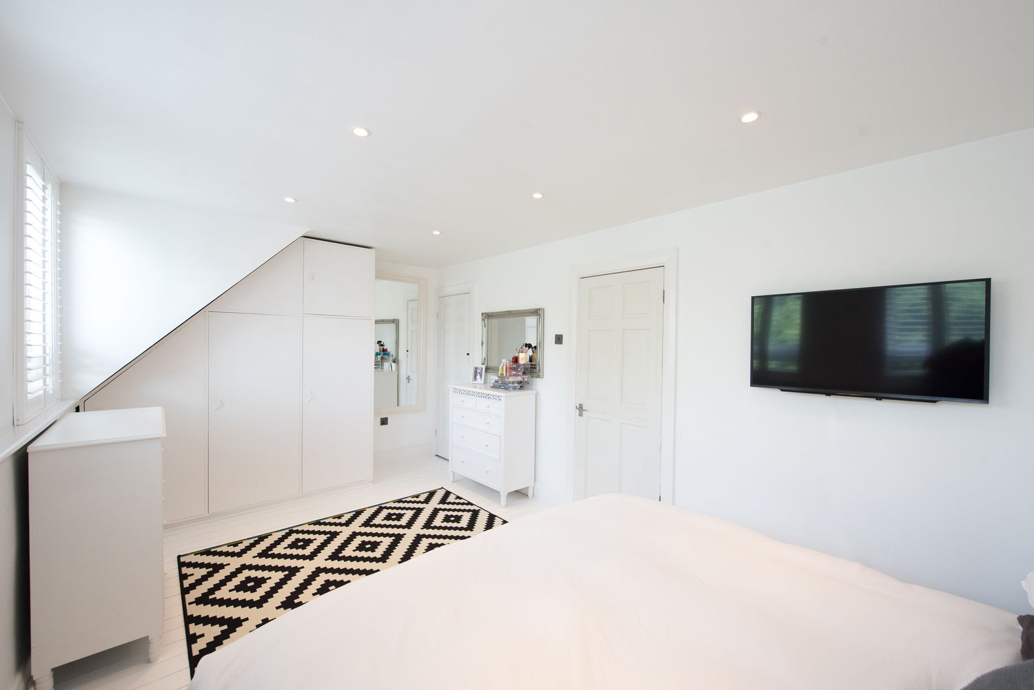 An der Wand montierter Fernseher in einem weißen Schlafzimmer