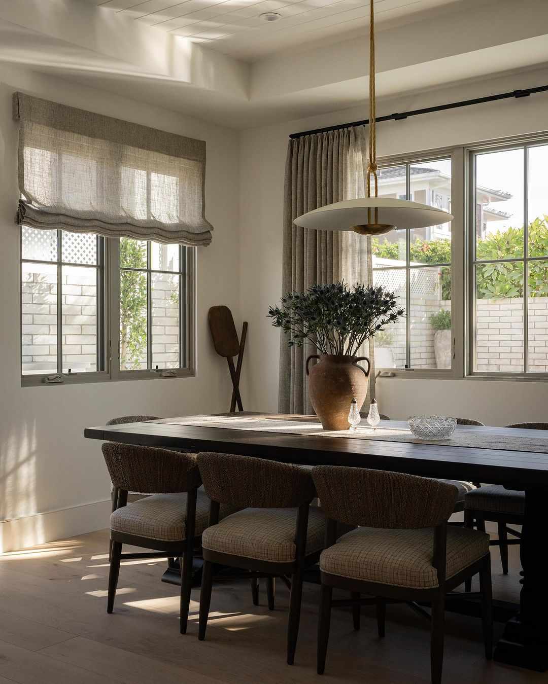 Modernes, rustikales Esszimmer mit industrieller, moderner Pendelleuchte, Bauernhoftisch, mit Rattan umwickelten Esszimmerstühlen und einer mit Disteln gefüllten Steinurne