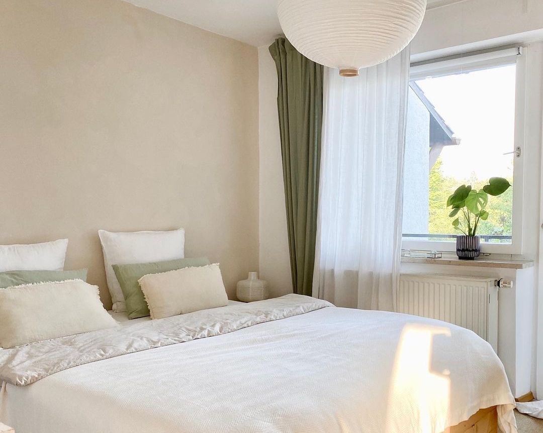 Ein strahlend weißes Schlafzimmer mit grün-weißen Vorhängen.