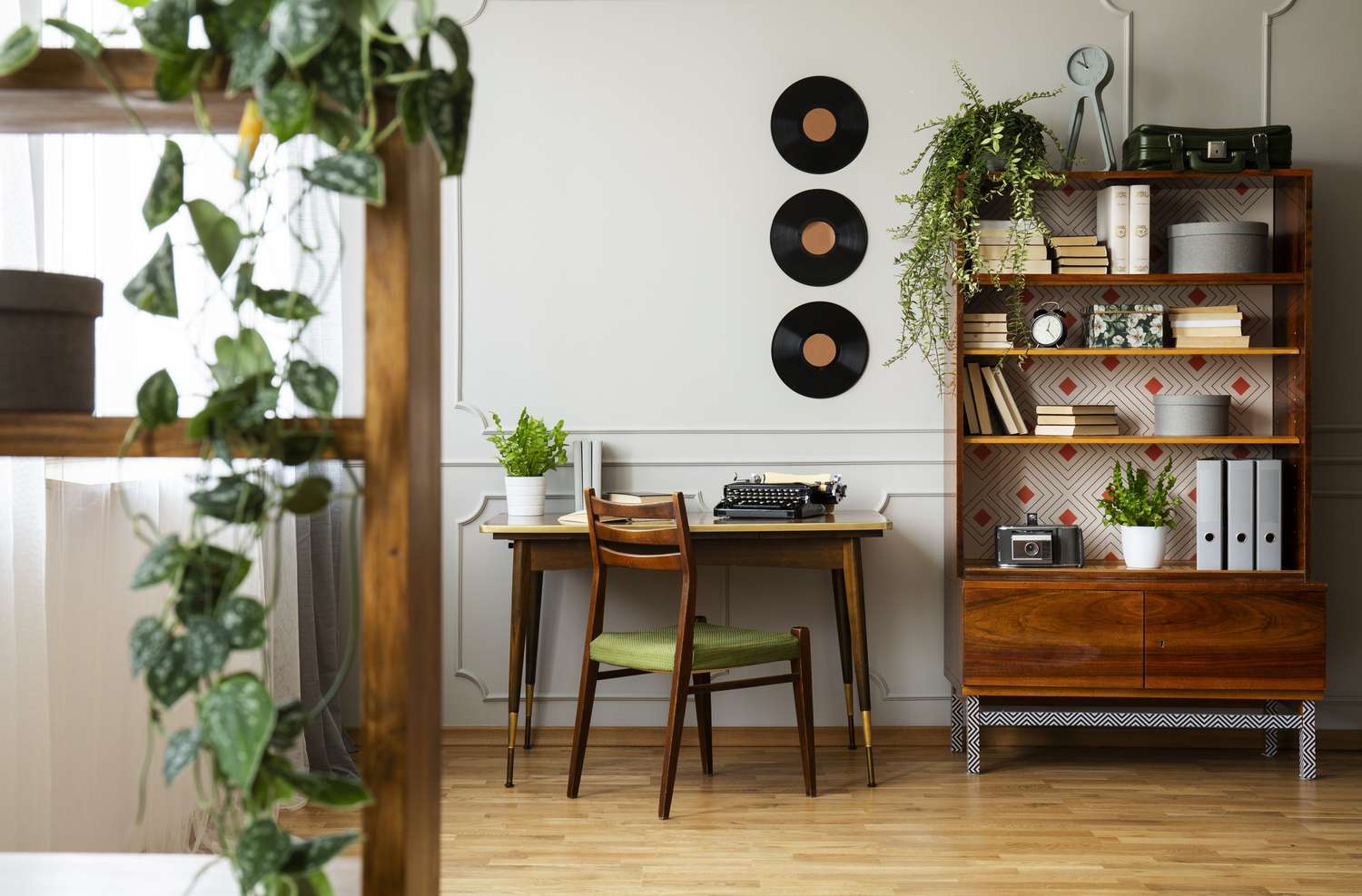 Schwarze Retro-Schreibmaschine auf einem einzigartigen Holzschreibtisch, ein Mid-Century-Modern-Stuhl und ein renoviertes Bücherregal in einem Hipster-Home-Office-Interieur.
