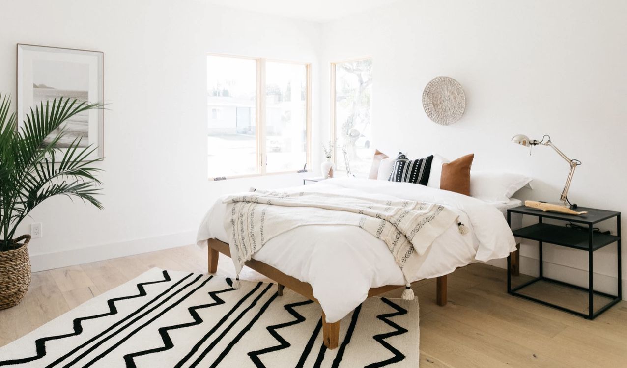 Minimalistisches Schlafzimmer mit Holzbettrahmen, große Pflanze in der Ecke
