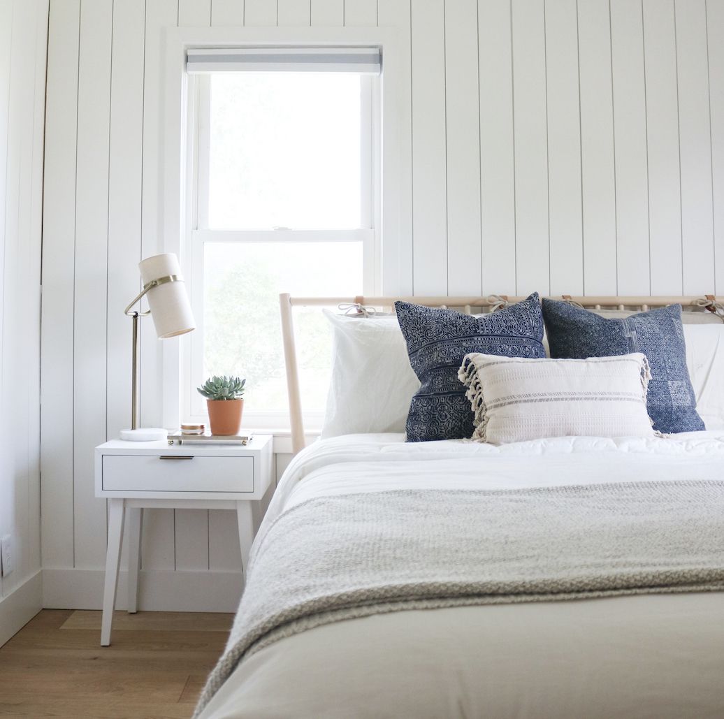 Weißes Schlafzimmer mit offenen Fenstern, blaue Akzentkissen auf dem Bett