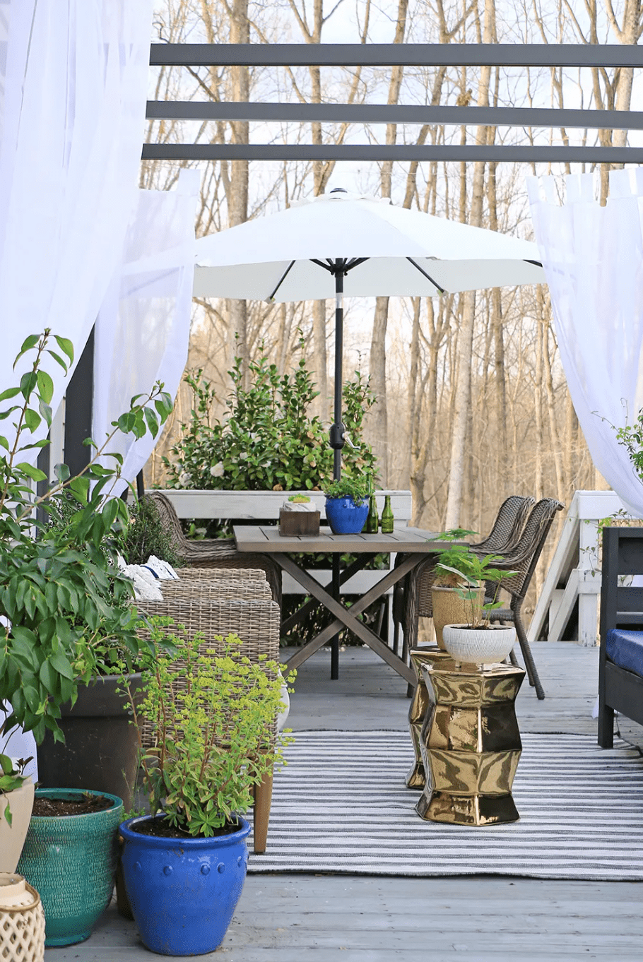 Eine mit Vorhängen, Pflanzen und einem passenden Terrassenmöbelset mit integriertem Sonnenschirm dekorierte Terrasse
