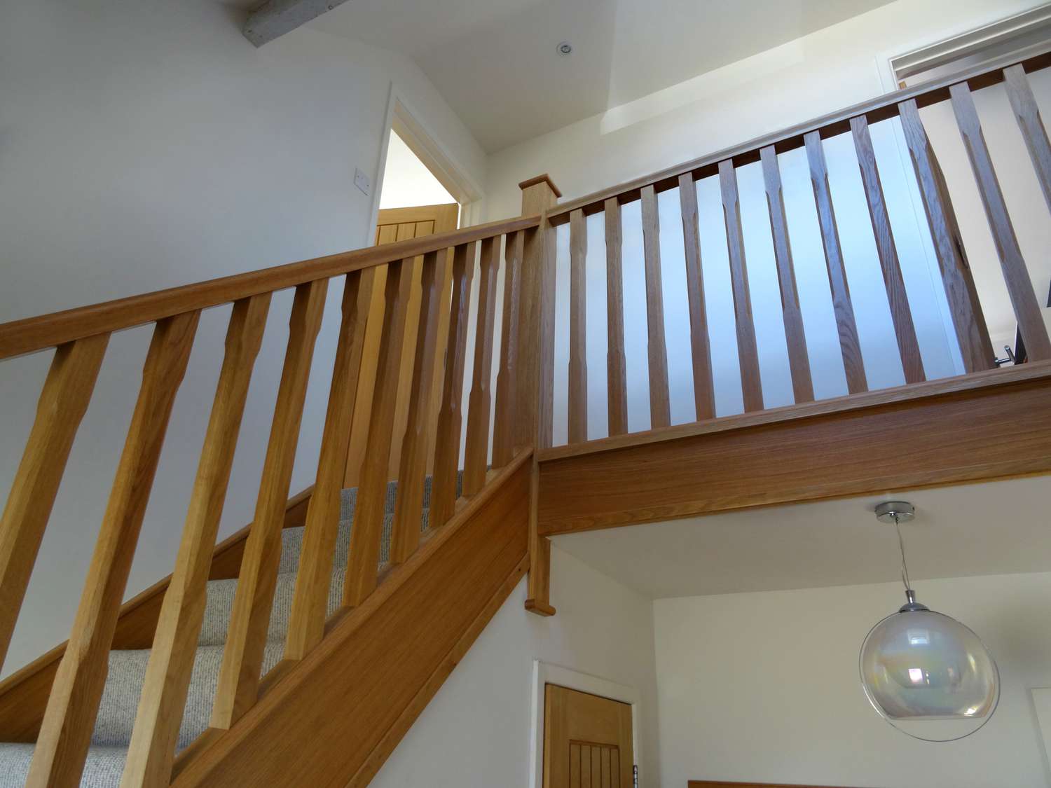 Was ist der Unterschied zwischen einer Balustrade und einem Baluster? 4 Das Foto zeigt einige moderne gerade Treppenspindeln/Balustraden aus hellem Eichenholz, die im Flur eines Wohnhauses abgebildet sind und einen großen Eingang schaffen. Diese Balustrade aus Eichenholz wurde gerade montiert, komplett mit passenden Handläufen, Sockelleisten und Fußleisten sowie einem hellbeigen, cremefarbenen Teppich auf den Stufen/Treppen.