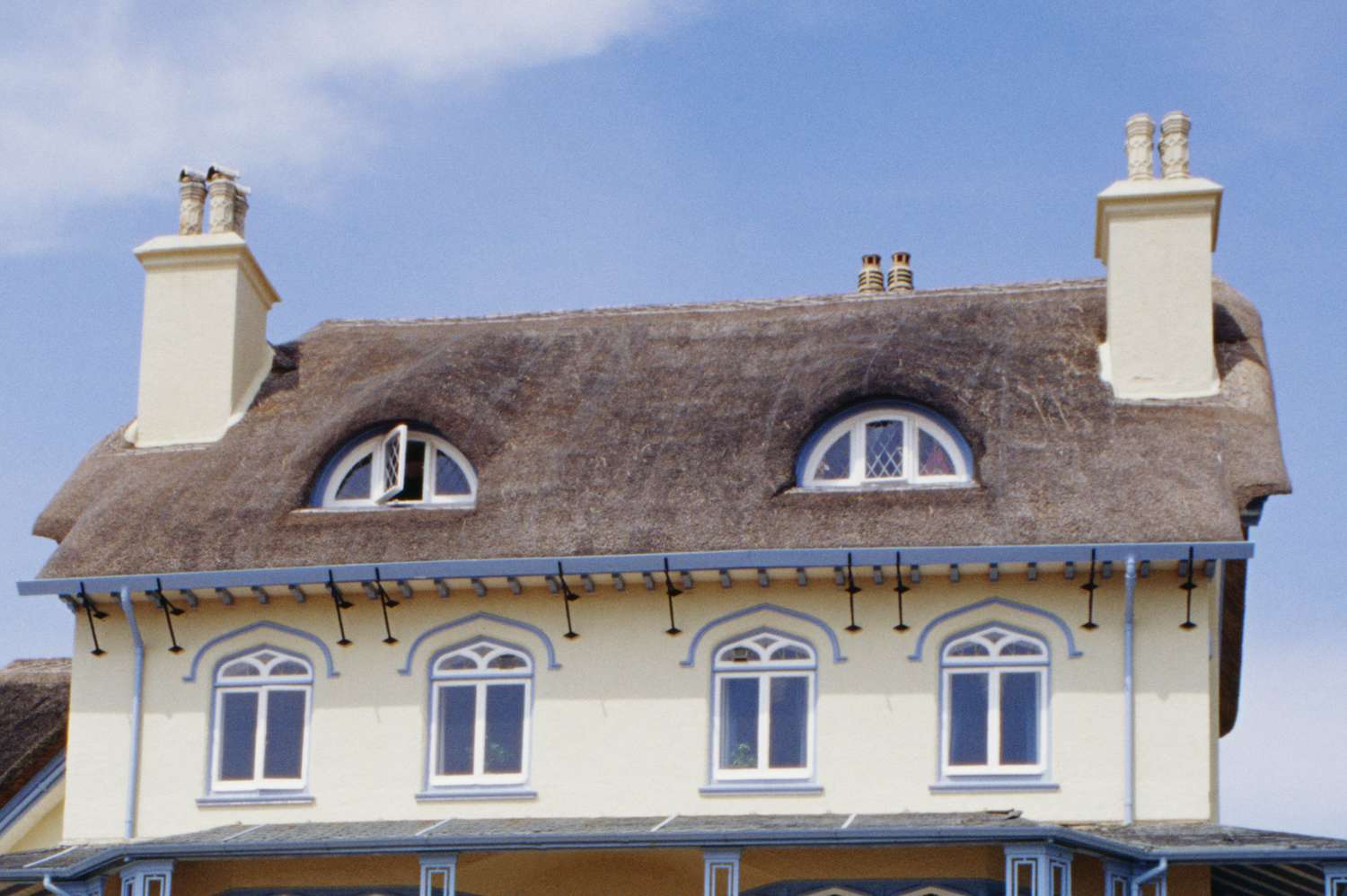 Blick auf den zweiten Stock und die Dachfassade, dreiteilige Rundbogenfenster auf einem Reetdach zwischen zwei riesigen Schornsteinen mit Schornsteinköpfen