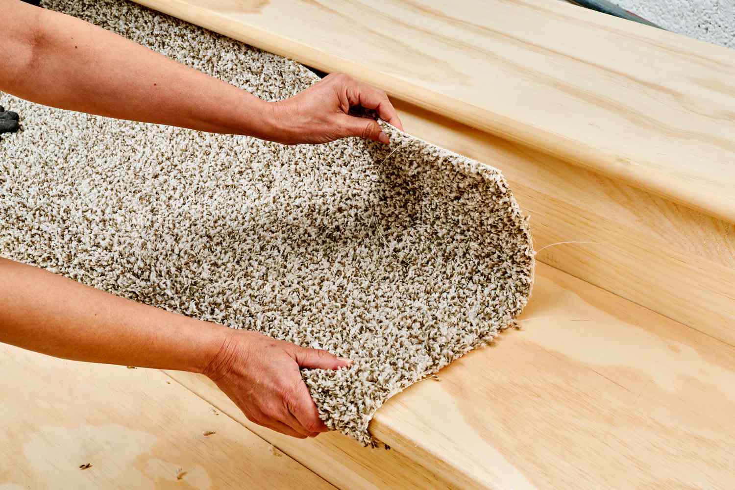 Person passt beigefarbenen Teppich auf Holztreppe an