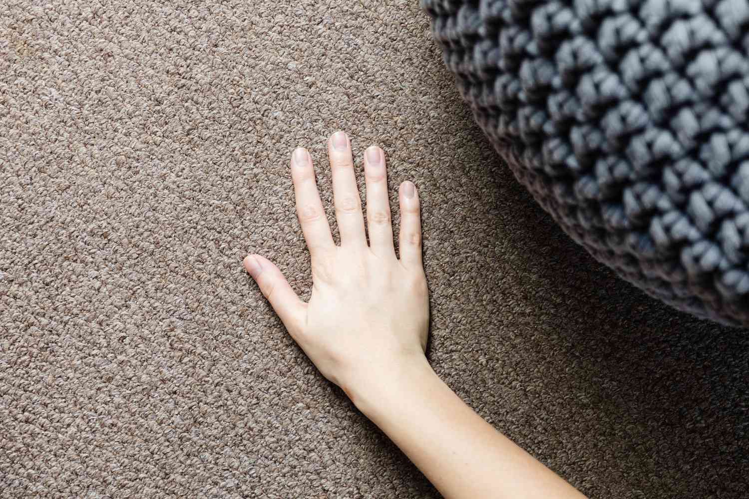 Hand geht über braunen Teppichboden neben grauem Hocker