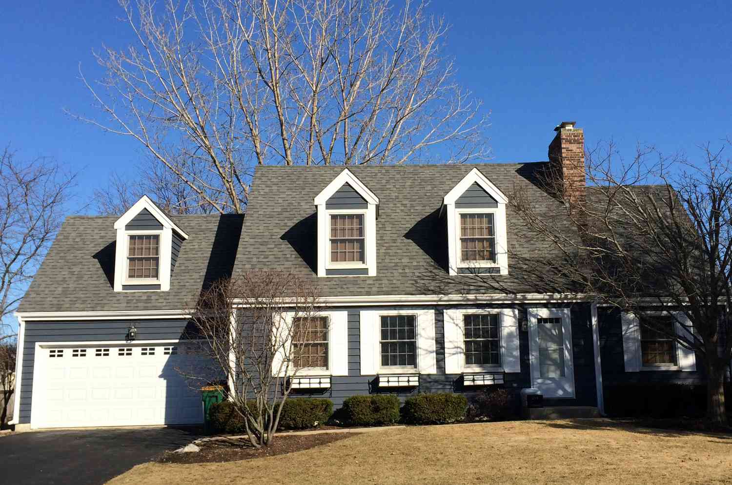 Haus im Cape Cod-Stil mit zwei Dachgauben am Haus und einer über dem Garagentor.