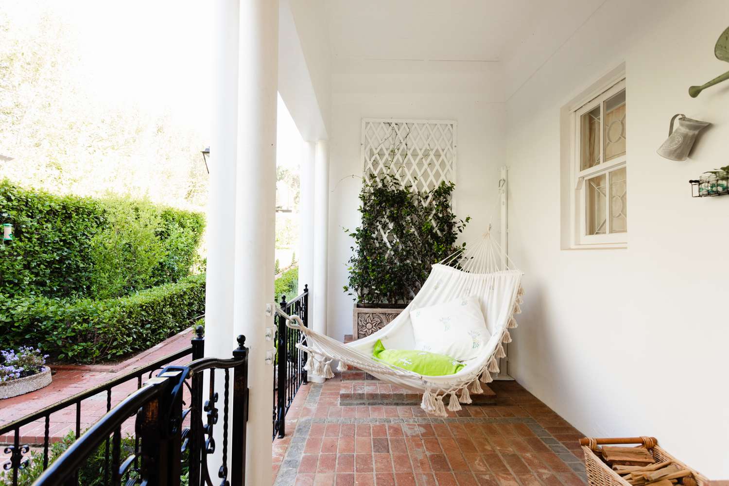 Veranda vs. Terrasse: Hauptunterschiede 2 Außenterrasse mit Ziegelboden und weißer Hängematte, die zwischen Wand und Säule hängt
