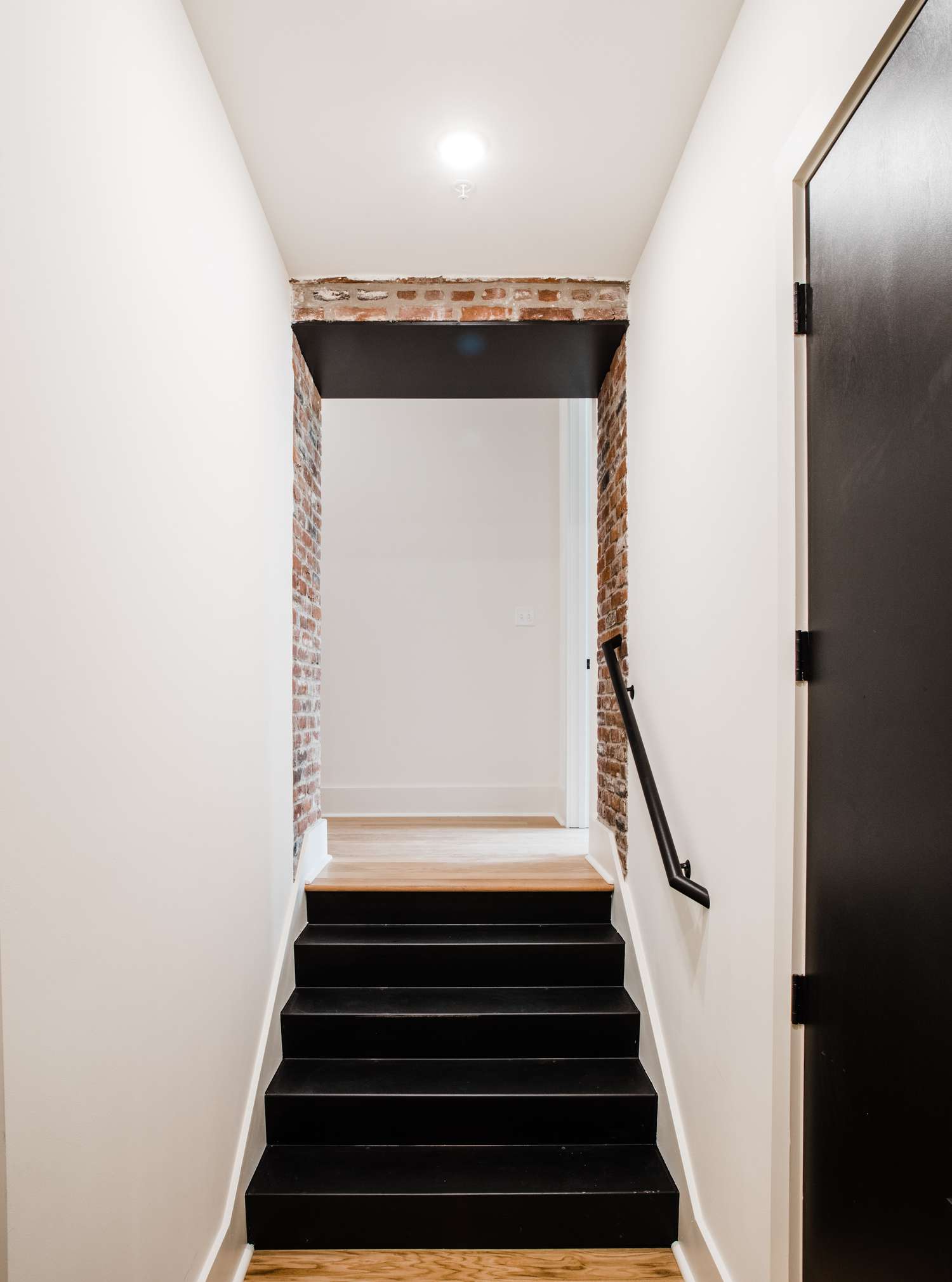 Schwarze Stahltreppe mit freiliegenden Ziegel und weißen Wänden.