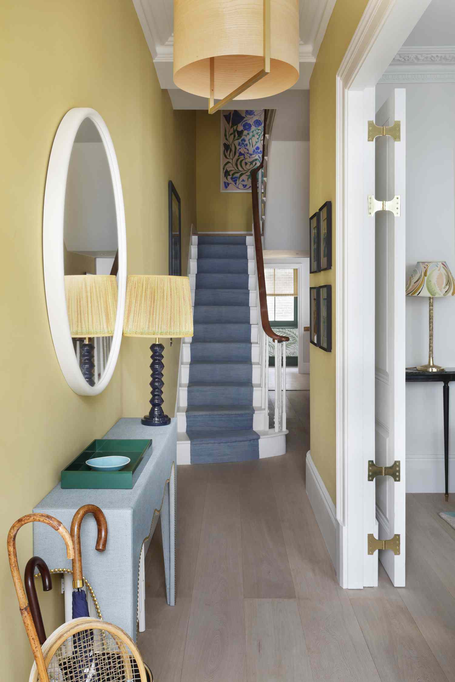 Yellow hallway with a round wall mirror above a console