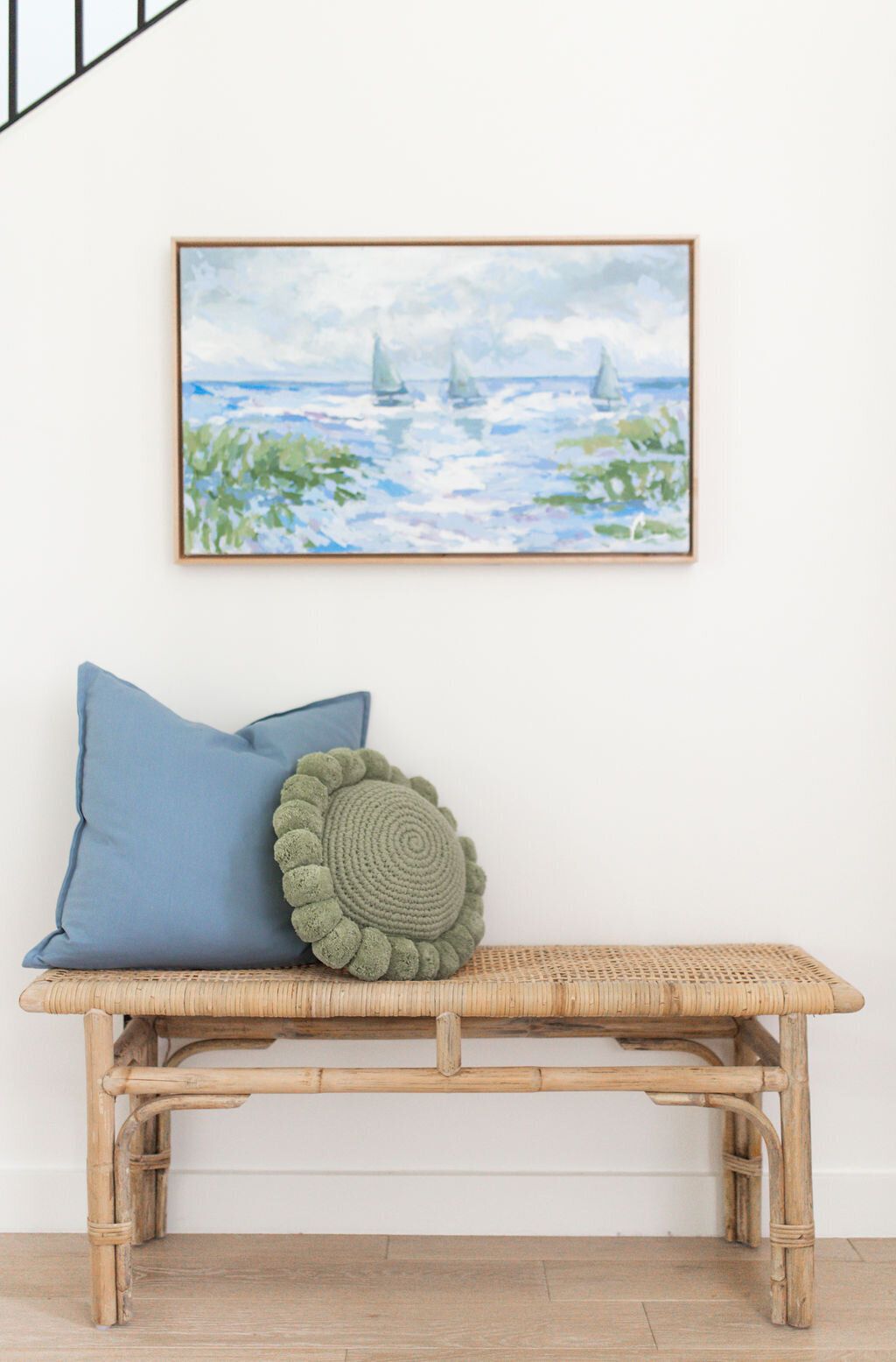 Wicker bench with pillows and a piece of art above it