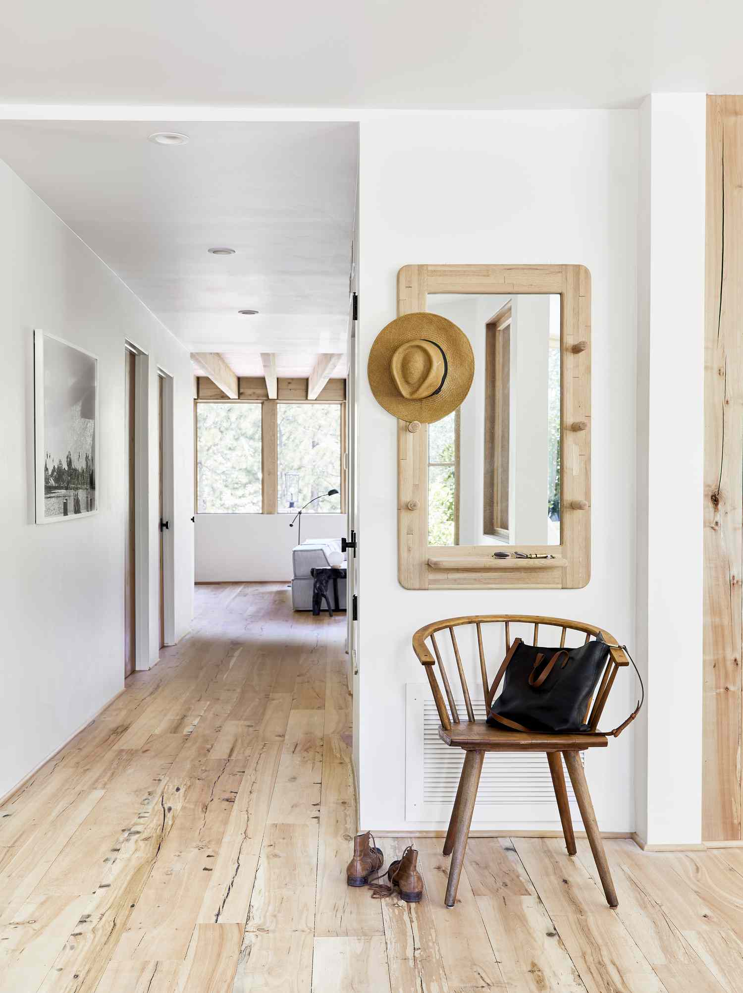 White hallway with wood floors and a chair and wooden mirror