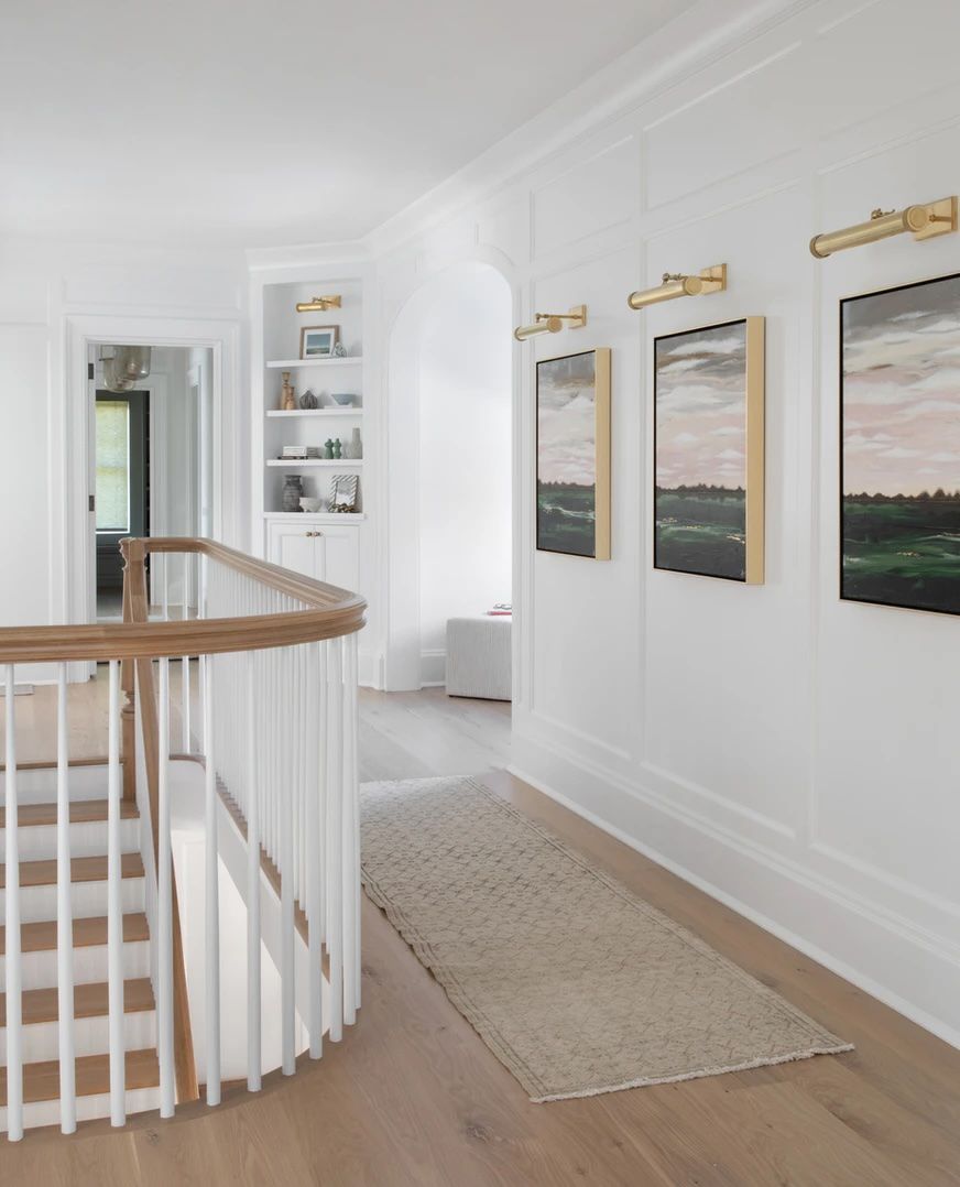 Corner bookcase and artwork with picture lights in a narrow hallway