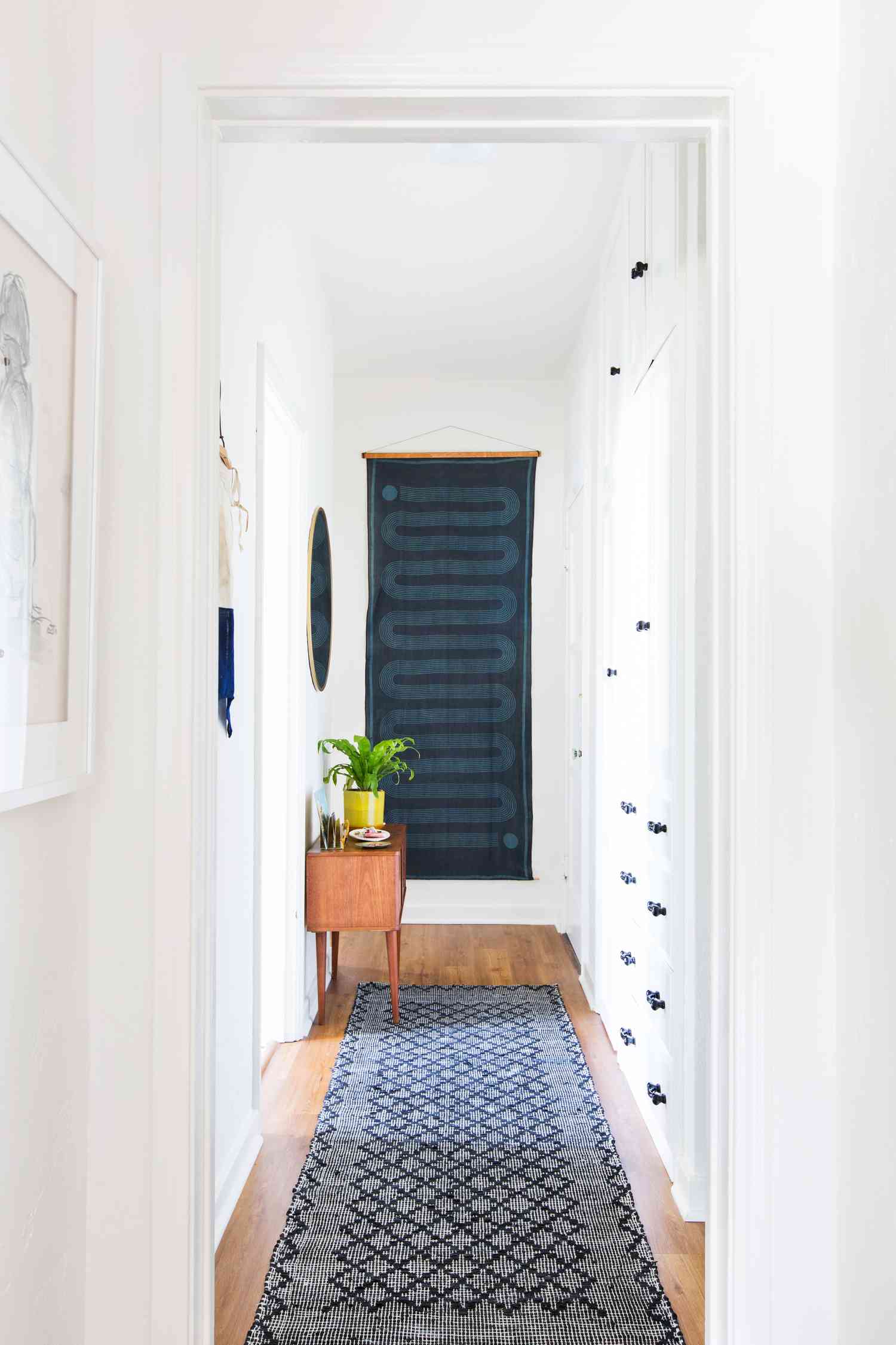 Narrow hallway with small wooden console and wall hanging at the end of the hallway