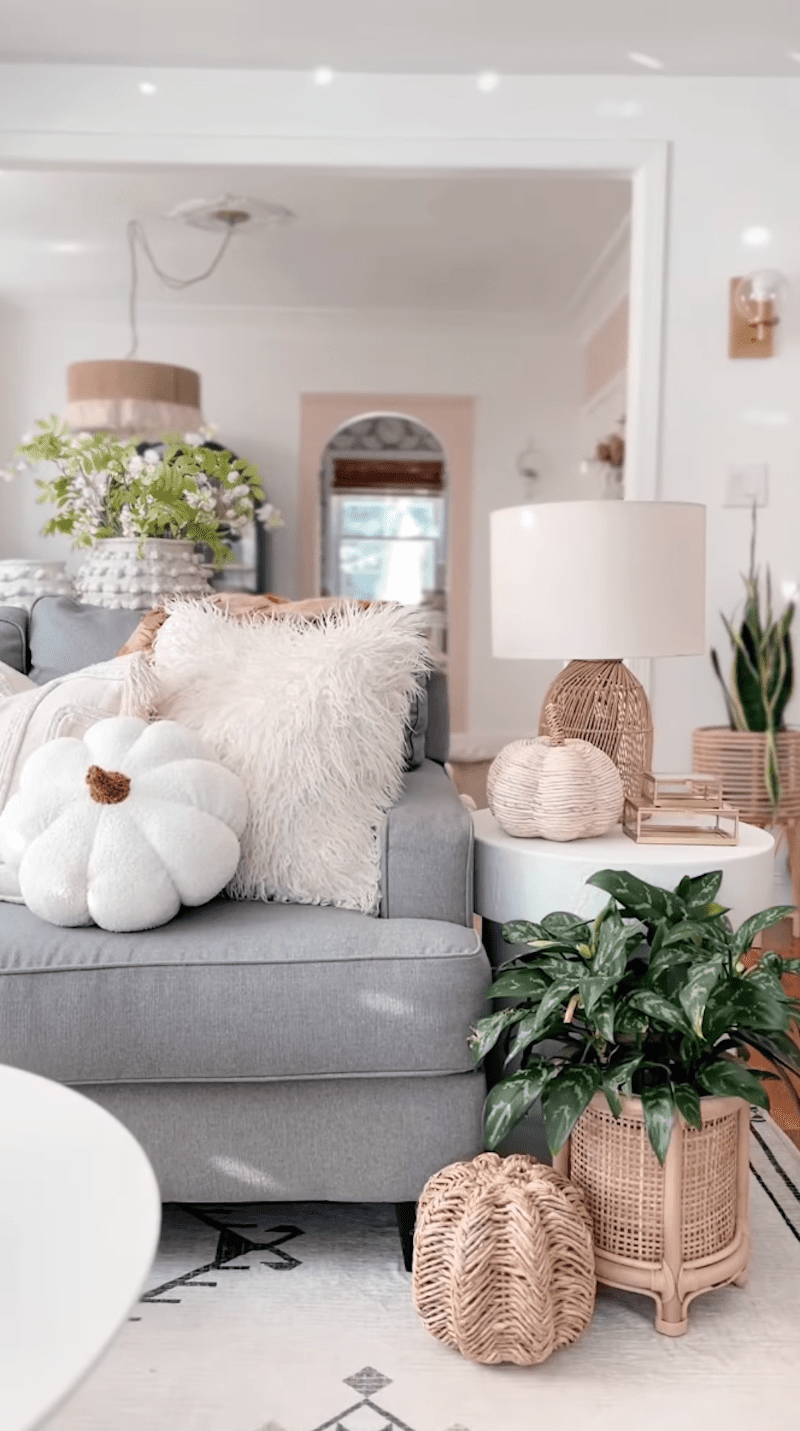 6 einfache Möglichkeiten, wie ich mein Zuhause für den Herbst vorbereitete, ohne einen Cent auszugeben 2 Eine Wohnzimmer -Couch mit einem weißen Kürbis -Wurfkissen gekrönt