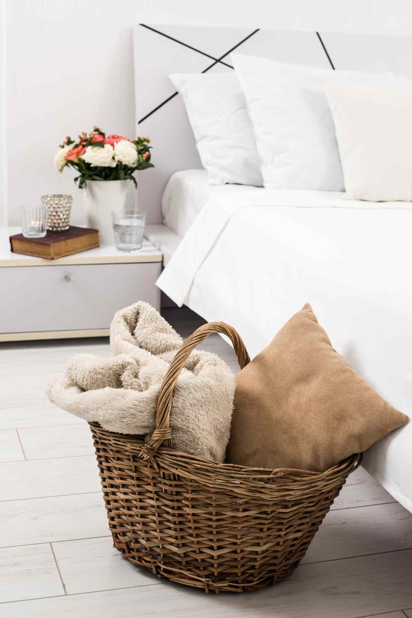 5 Dinge, die ein Designer nie aus dem Gebrauchtwarenladen kauft (und Sie sollten auch nicht) 12 Innenraum des weißen Schlafzimmers, neue Bettwäsche auf dem Bett, gemütliches Zuhause. Weidenkorb und Kissen Nahaufnahme.