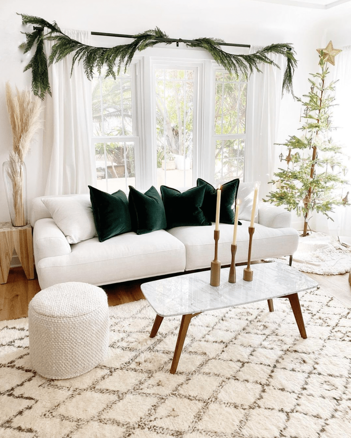 A living room decorated with a thin Christmas tree, three gold candlesticks, and an evergreen garland