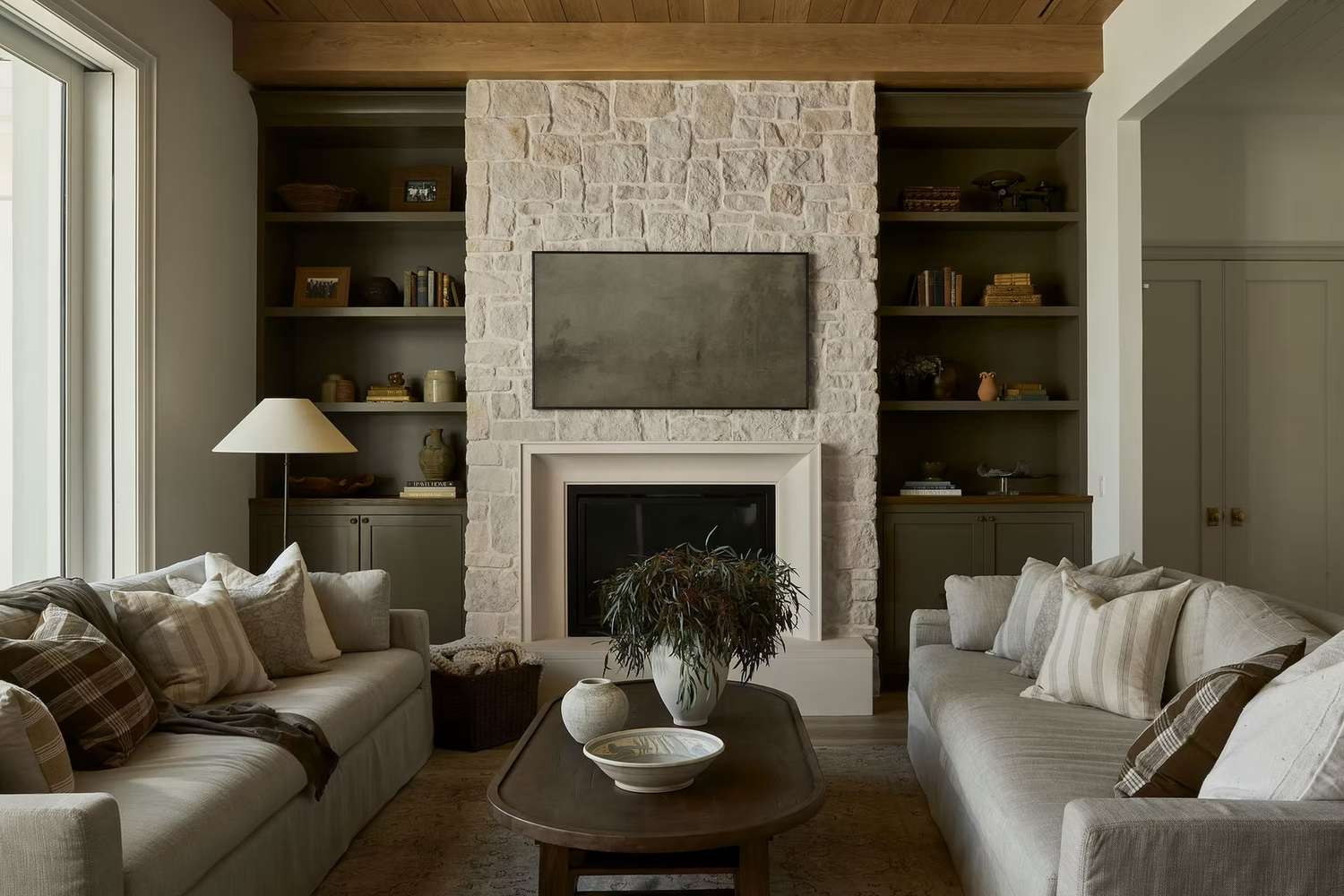 Lange Wohnzimmer können verwirrend sein, aber diese 7 Tipps von Designern können helfen 16 Ein neutrales Wohnzimmer mit symmetrischen Doppelsofas und vertikaler olivgrüner Regale auf beiden Seiten eines Steinkamins