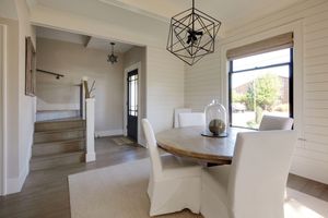 5 Dekoration Fehler, die Ihr Zuhause laut Designer sich heißer fühlen lassen 4 Ein elegantes Essaufbau mit weißen Stühlen um einen stilvollen Tisch, eine Vordertür -Kulisse und eine Treppe, die auf ein luxuriöses traditionelles Hüttenbiente hinweisen.