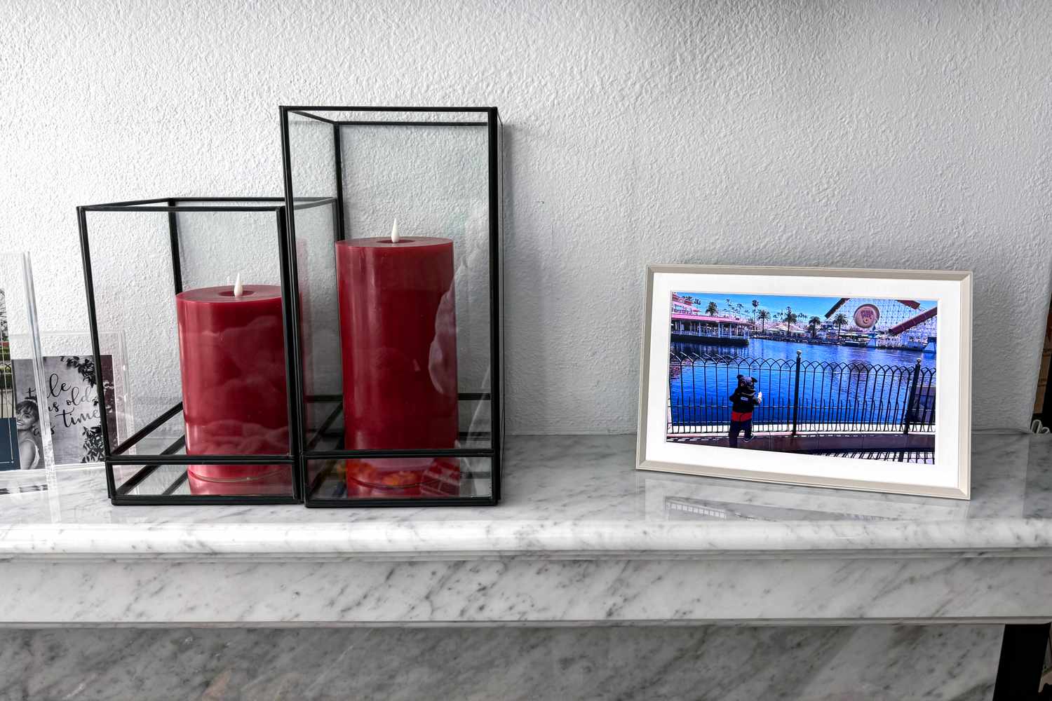 Ein Paar rote Kerzen in geometrischen Ständern neben dem digitalen Fotorahmen der Aura Carver auf einer Marmoroberfläche