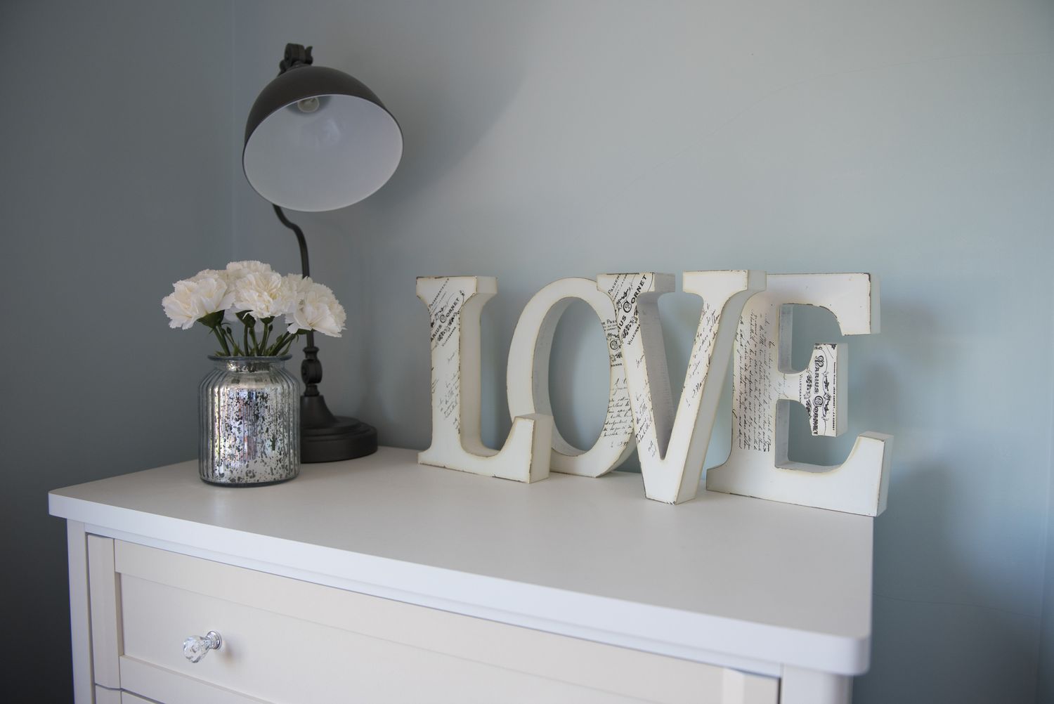 5 Dekorakzente Designer sagen, dass sie gerade weit übertrieben sind 8 Eine allgemeine Sicht auf eine Truhe aus Schubladen, die mit einer Tischlampe verziert ist. Blumenvase und individuelle Buchstaben, die das Wort Liebe in einem Schlafzimmer in einem Familienhaus buchstabieren