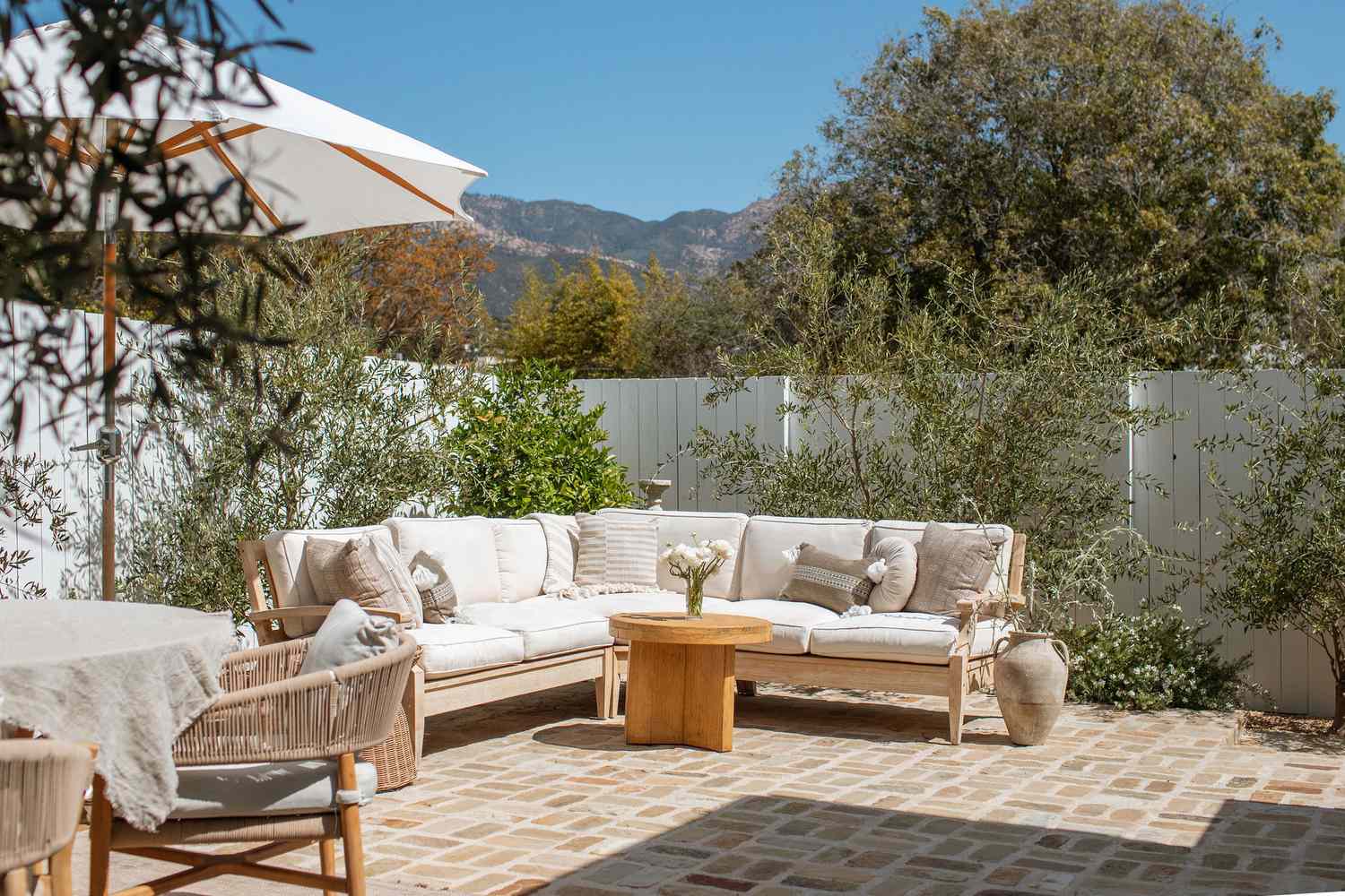 6 Backyard -Privatsphäre Korrekturen, die sich ohne den Preis luxuriös fühlen, sagen Designer, sagen Designer 10 Kalifornischer Mittelmeer Hinterhof mit weißen Sektion im Freien, die von Olivenbäumen unterstützt werden