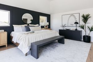 Dekoriertes Schlafzimmer mit dunkelblauen Wänden, Kommoden und Bank, die ein weißes Bett umgeben