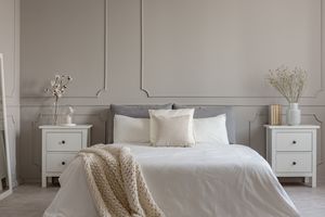Blumen auf weißem hölzernen Nachttisch im Luxus -Schlafzimmer -Innenraum mit Kingsize -Bett