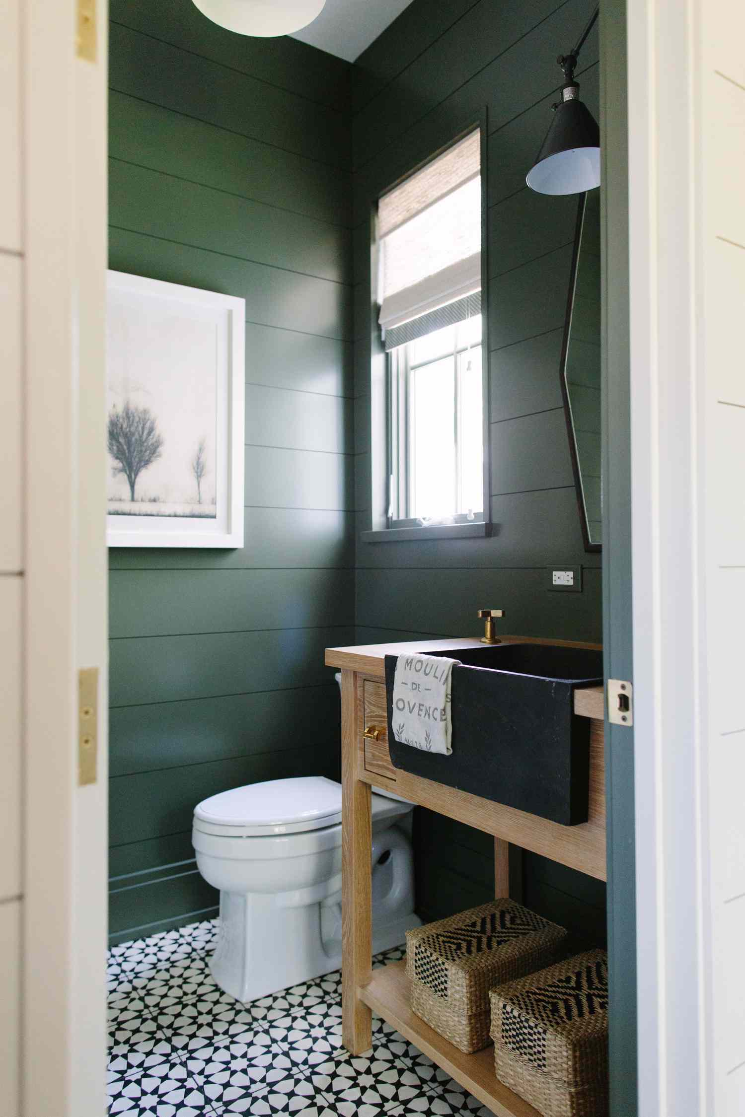 A dark green bathroom with a black farmhouse sink and wood vanity