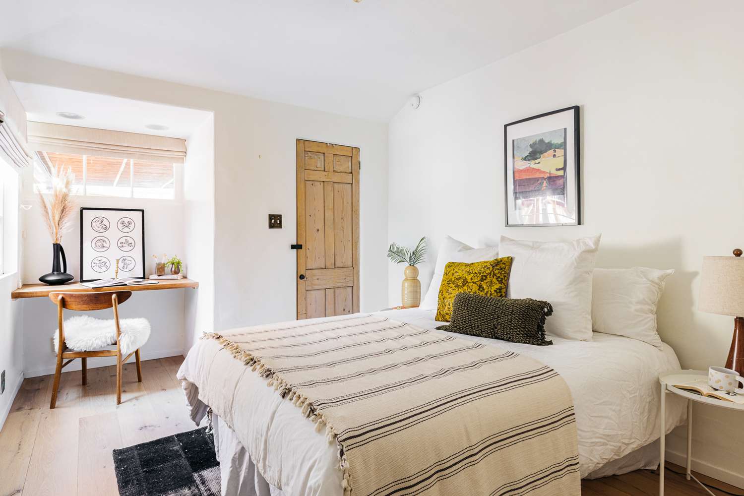 Small bedroom with striped throw blanket on bed and decorated office desk corner